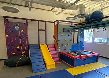 A gym with fitness balls, rings, swings, a pit, stairs, a slide, and a climbing wall.